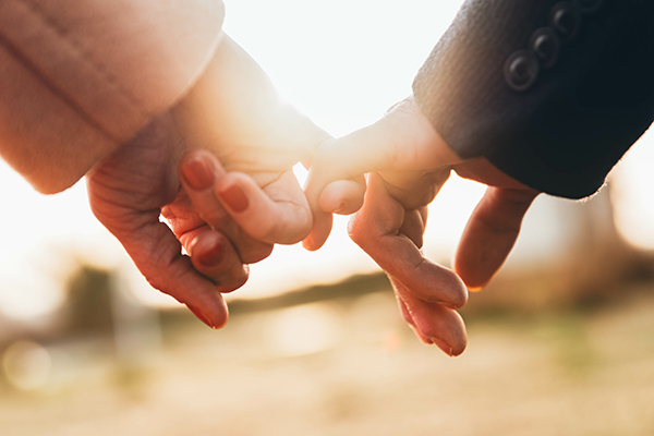 Two people holding hands by their pinky fingers