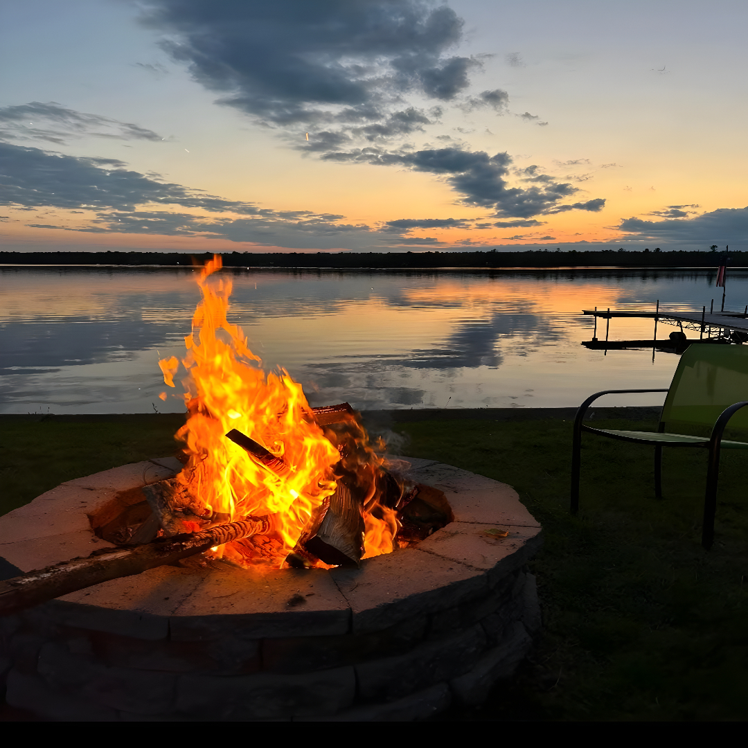 A fire pit blazing on a sandy beach at sunset.