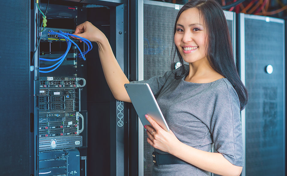 A woman standing at a mainframe looking at the camera