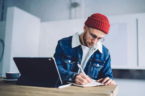 Male in red beanie takes notes during online class