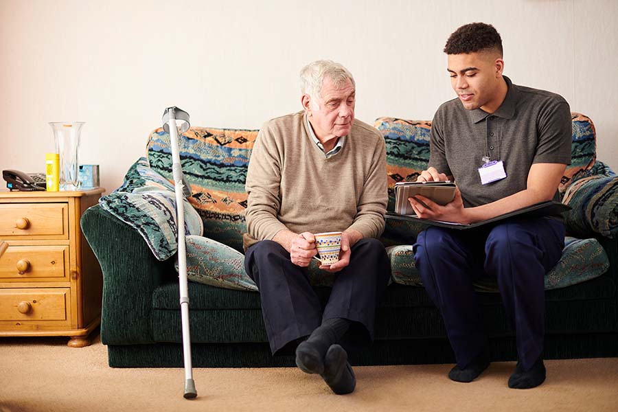 senior man with caregiver at home sitting on couch