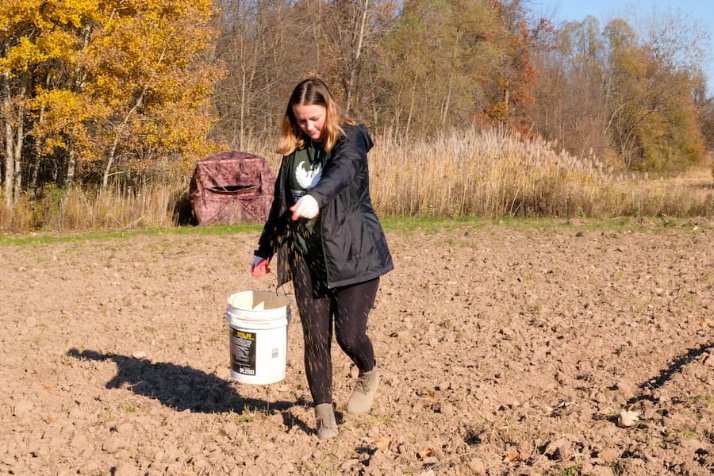 Student sprinkles seeds on plowed field