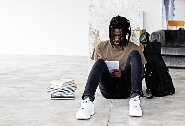 Black male student leans against column while studying.