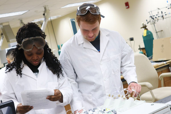 Two students in lab coats and safety goggles