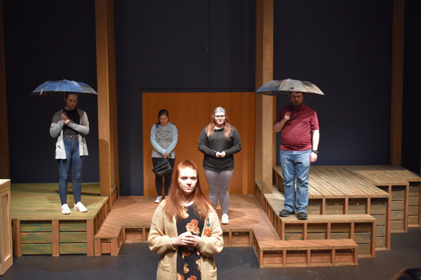 Students hold umbrellas on stage during This Random World performance