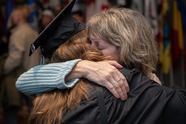 Student in cap and gown hugs her mom at commencement