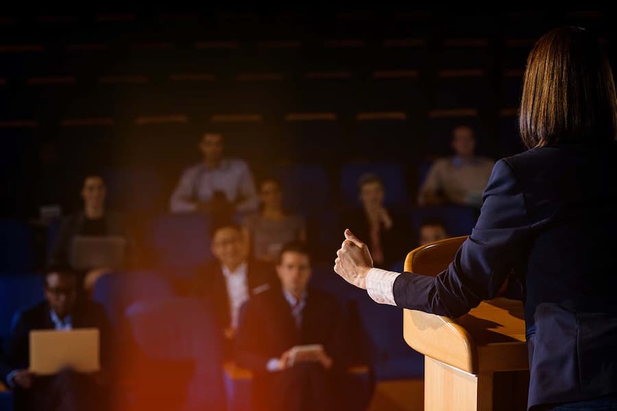 view from behind of woman speaking at conference