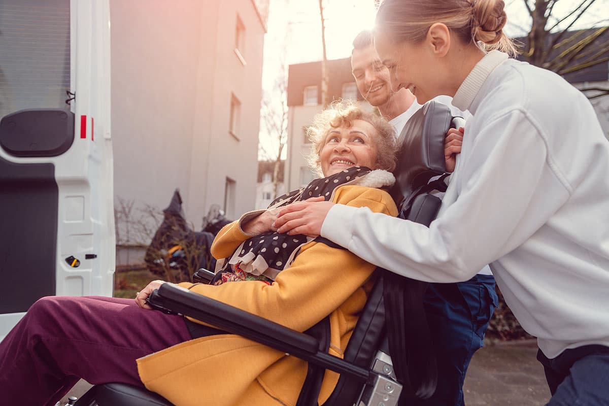 Caregivers helping elderly woman into transportation vehicle