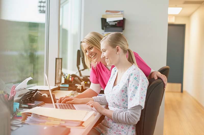 two caregivers sitting by laptop in assisted living facility