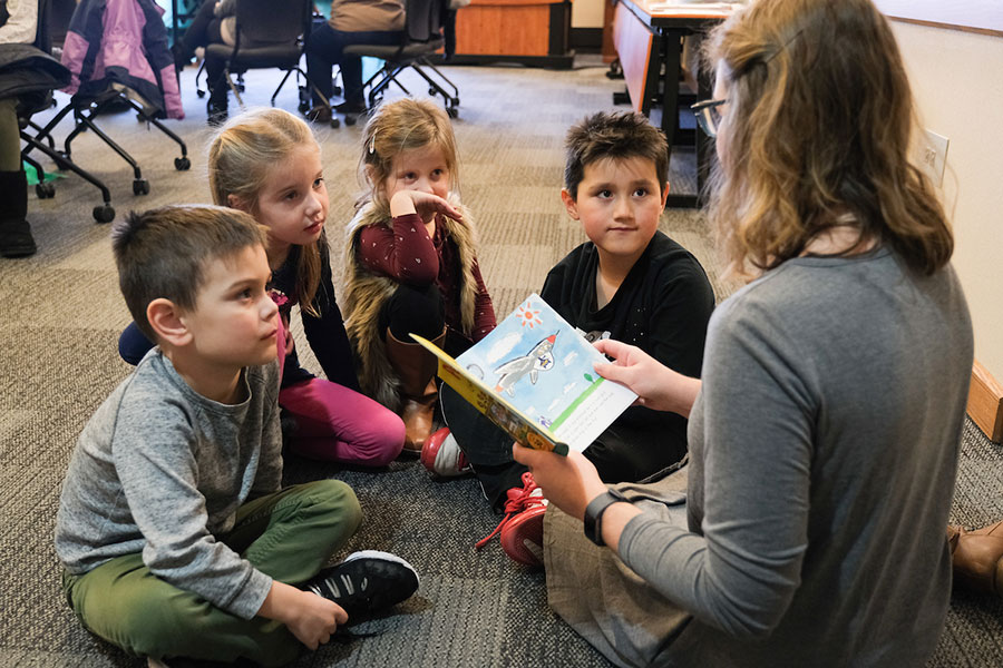 Teacher sitting and reading to a group of young students.