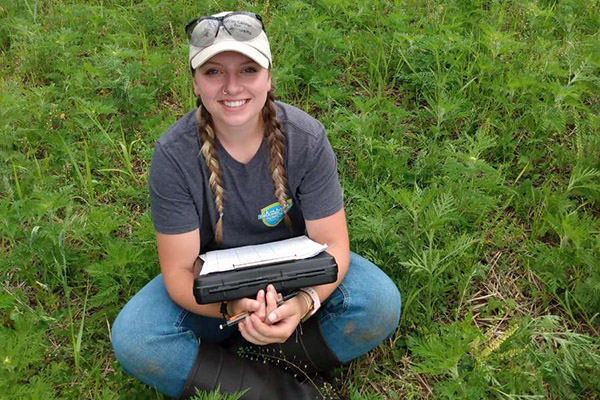 Haillee Fritsch seated in a field, holding a clipboard box