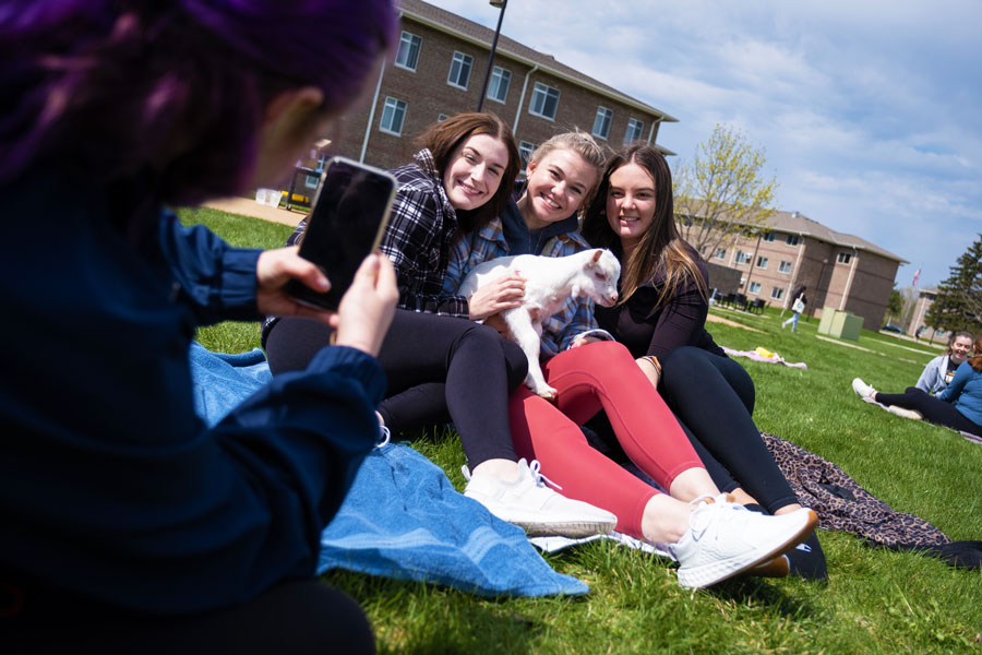 Student takes picture of three students holding goat at goat yoga