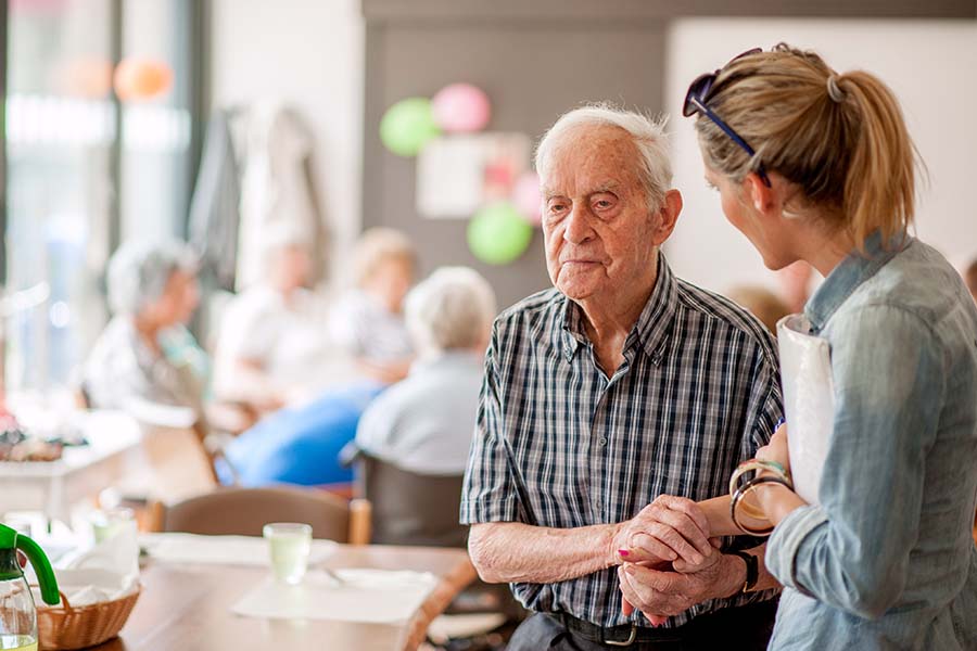 woman caregiver helping an elderly man walk at assisted living facility