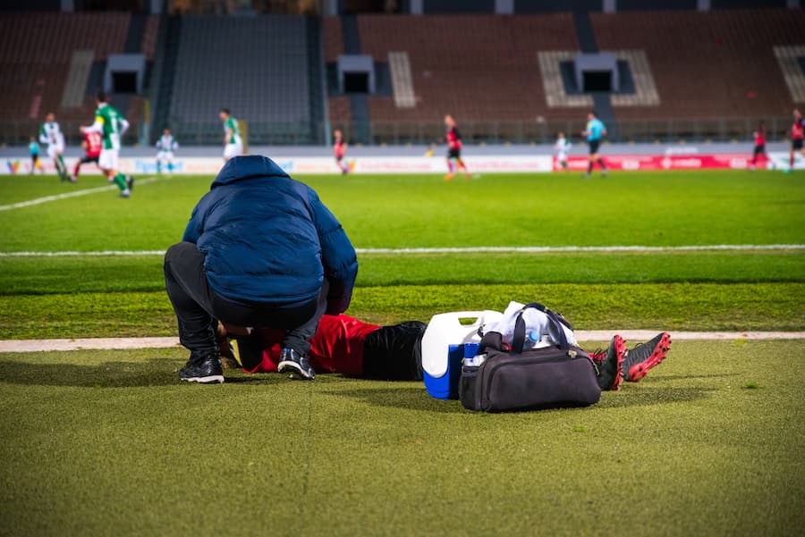 Athletic trainer helps injured athlete on the field