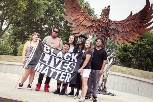Graduate posing with friends and Black Lives Matter banner