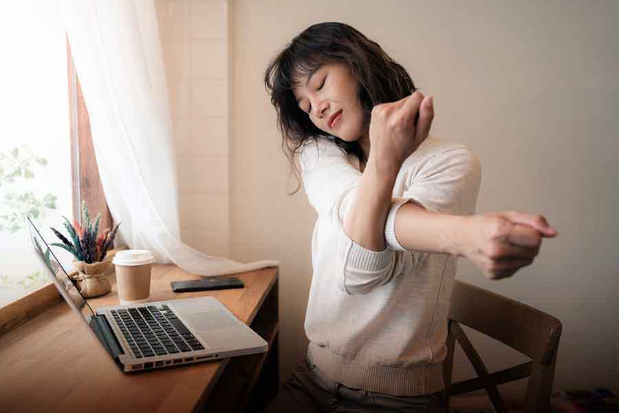Young woman stretching shoulders at computer desk