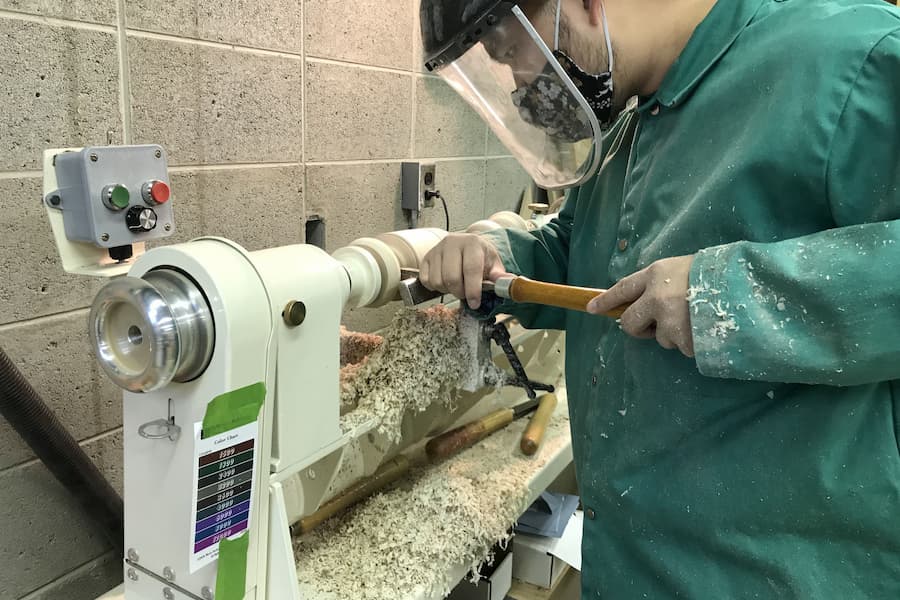 Student carves table leg in woodshop studio