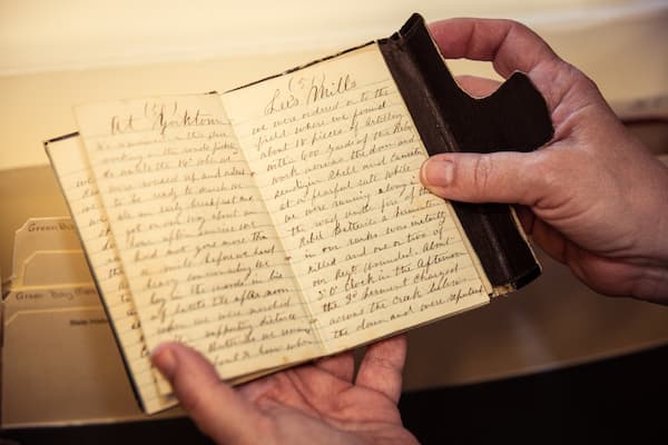 Hand holding a primary source artifact hand-written diary book from UW-Green Bay Archives