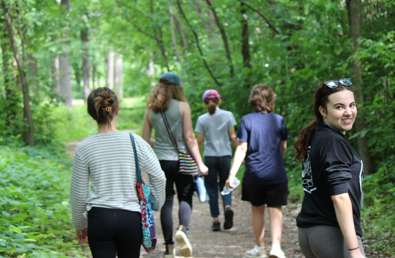 Group of students walking through woods. Girl looking back at camera