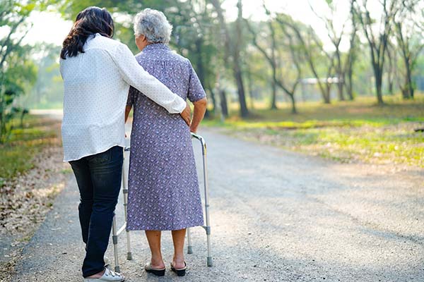 senior woman walking outside with walker and caregiver's help