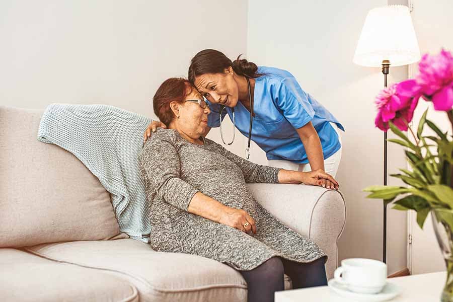 caregiver wearing blue scrubs leaning down comforting a senior woman