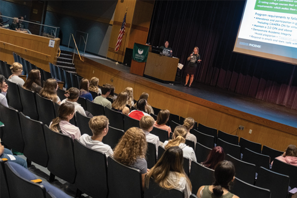 Students listening to a speaker in an auditorium.