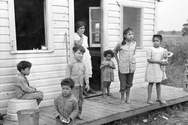 1984 A Mexican woman and her six children are standing on the porch of the multiple-family housing provided to them by the pea cannery for which their husband and father works. Courtesy of the WI Historical Society