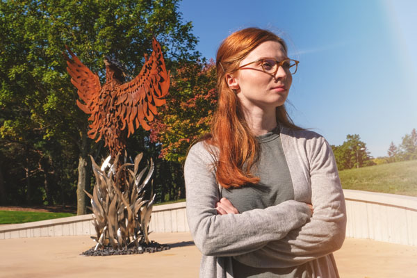 Female student poses with arms crossed in front of Pheonix Sculpture