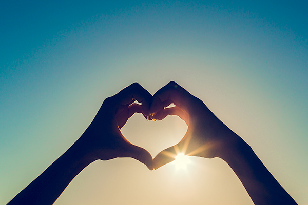 Hands making heart shape with sun behind