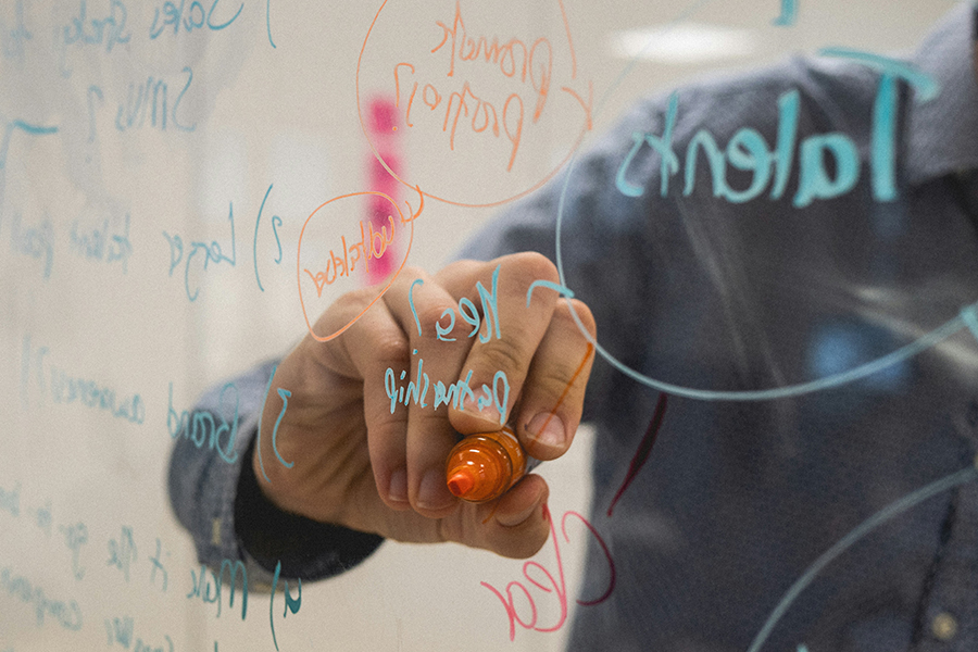 A hand writing on transparent glass with a dry erase marker