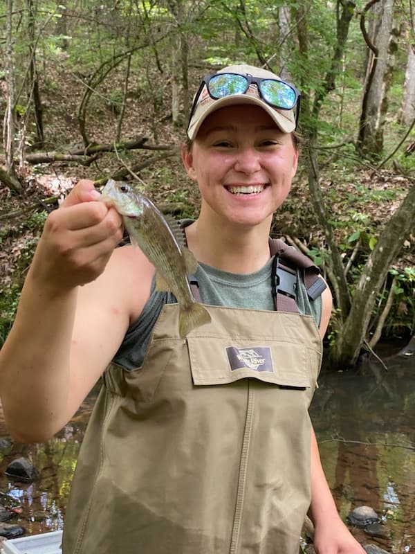 Claire Stuart wearing bib waders ni a stream, holding a fish