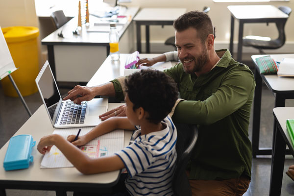 Teachers helps young student at desk