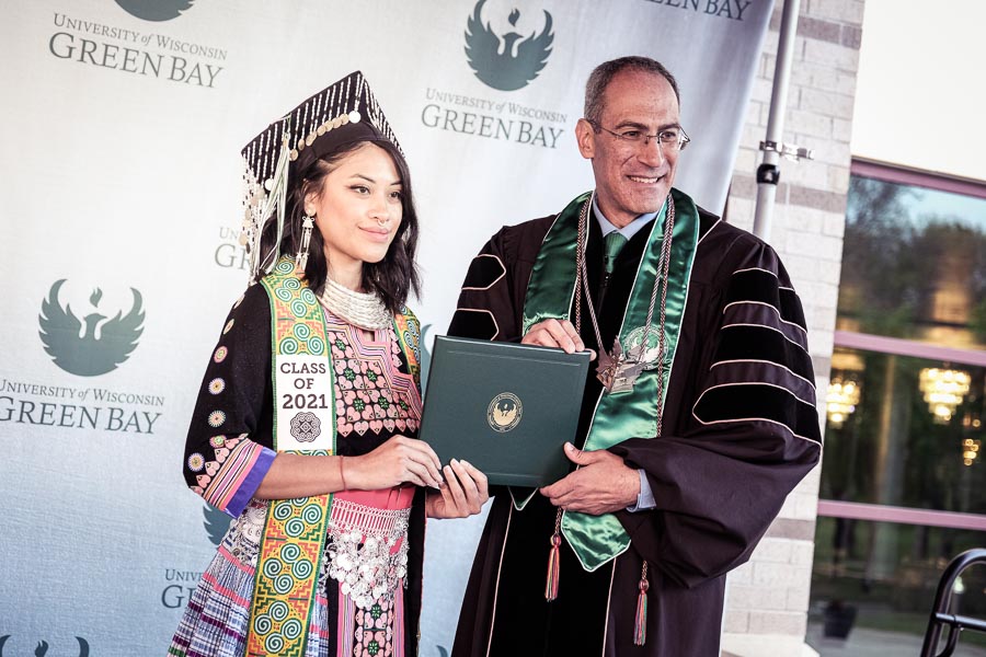 Chancellor Mike Alexander posing with a graduate with traditional adornments