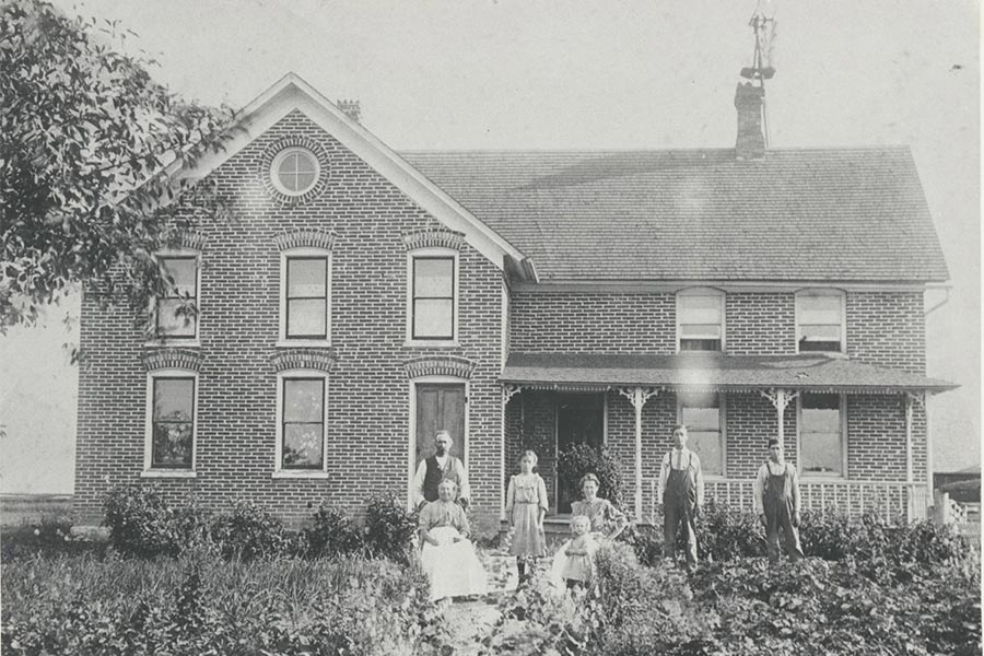 Black and white photo of a Belgian American farmhouse with family standing near the entrance