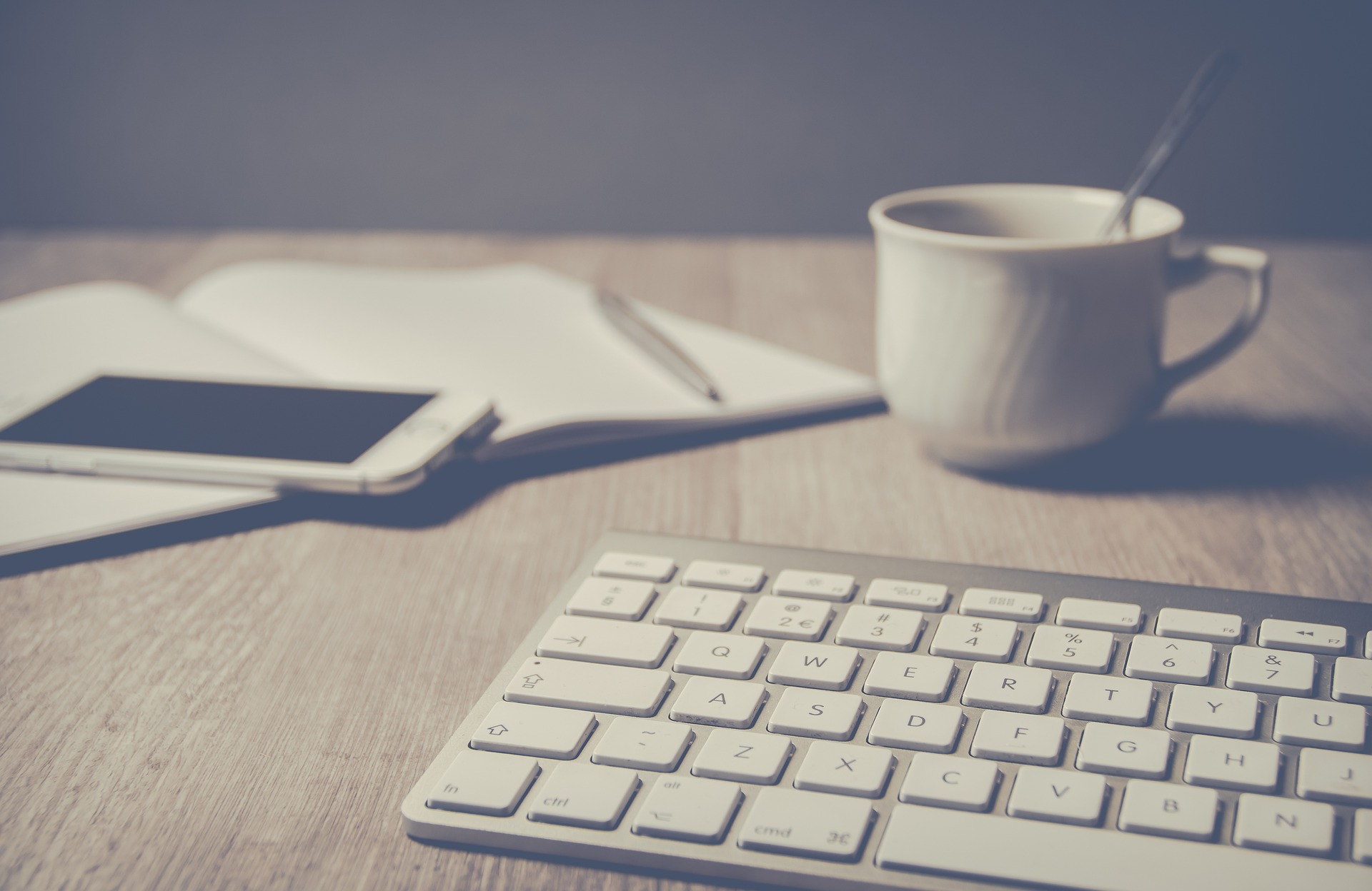 image of a keyboard, tea cup, notebook, pen and cell phone