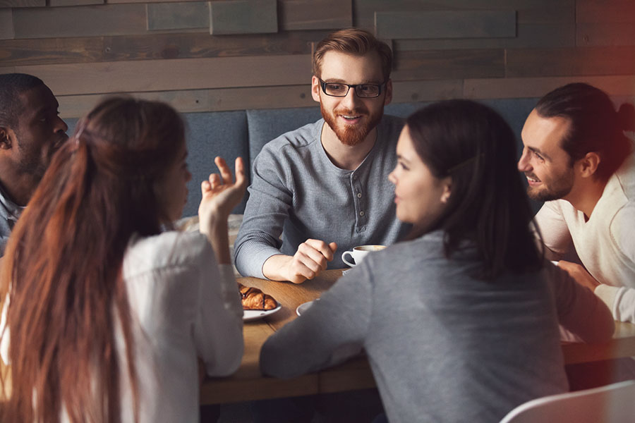 group of two men and three women sitting at a table talking