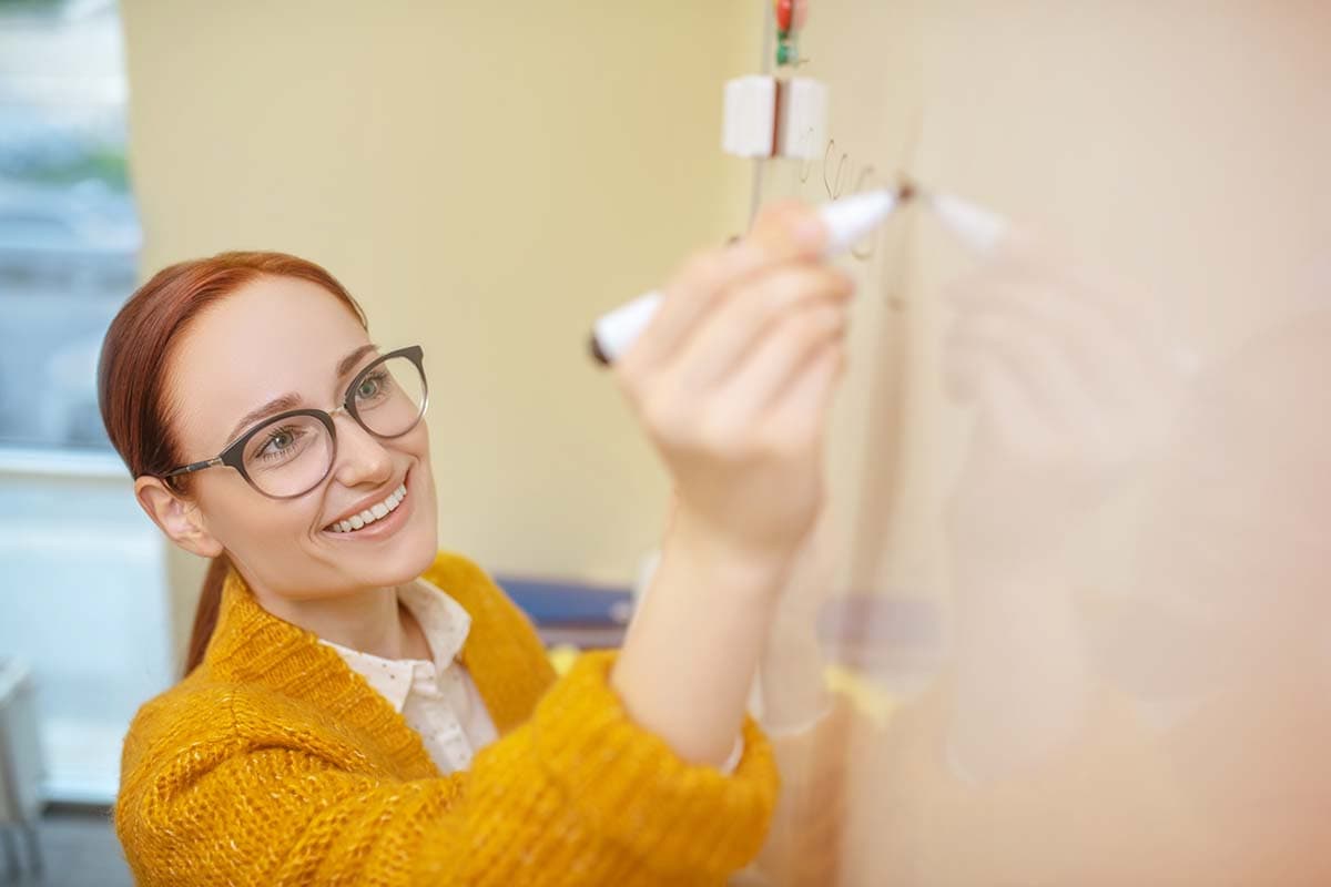 smiling teacher wearing yellow writing on marker board