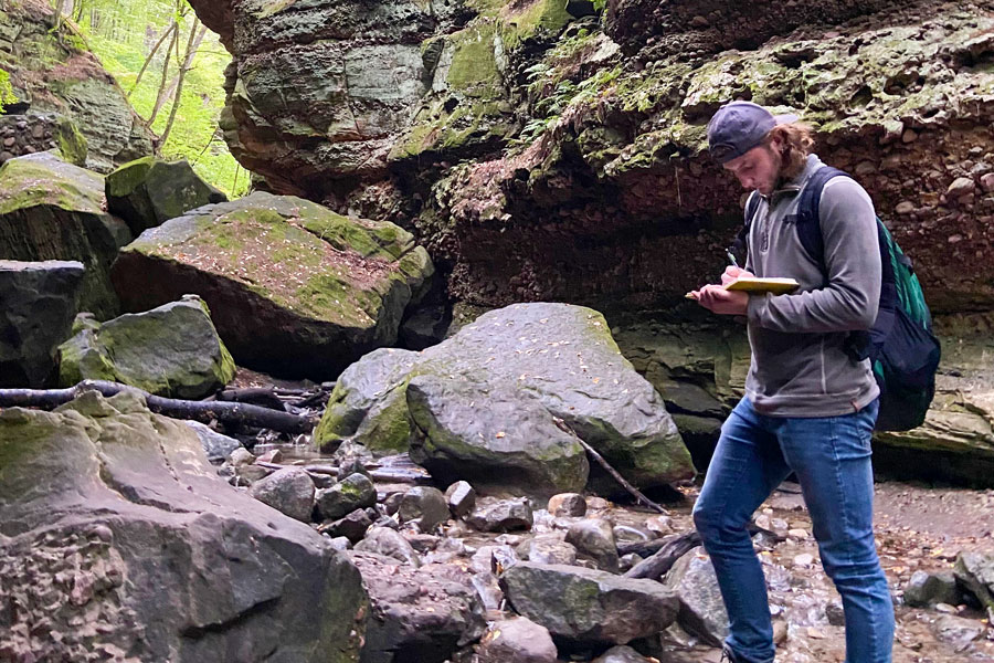 Geoscience student taking notes while studying large rock formation