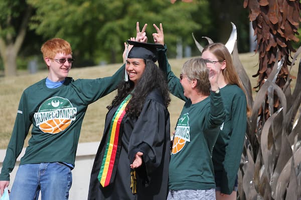 Graduate posing with friends in front of the Phoenix Rising sculpture