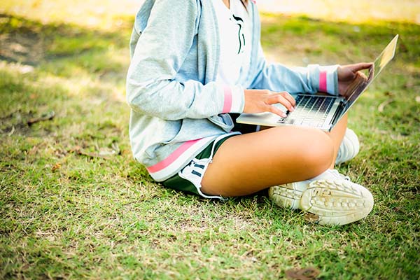 girl sitting outside on grass with laptop