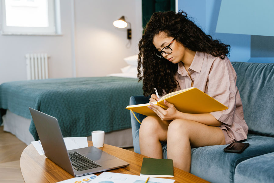 Female sitting on couch and taking notes during online class