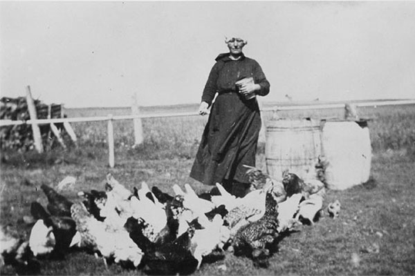 Black and white photo of Belgian American Zelia Wautlet feeding chickens on her farm