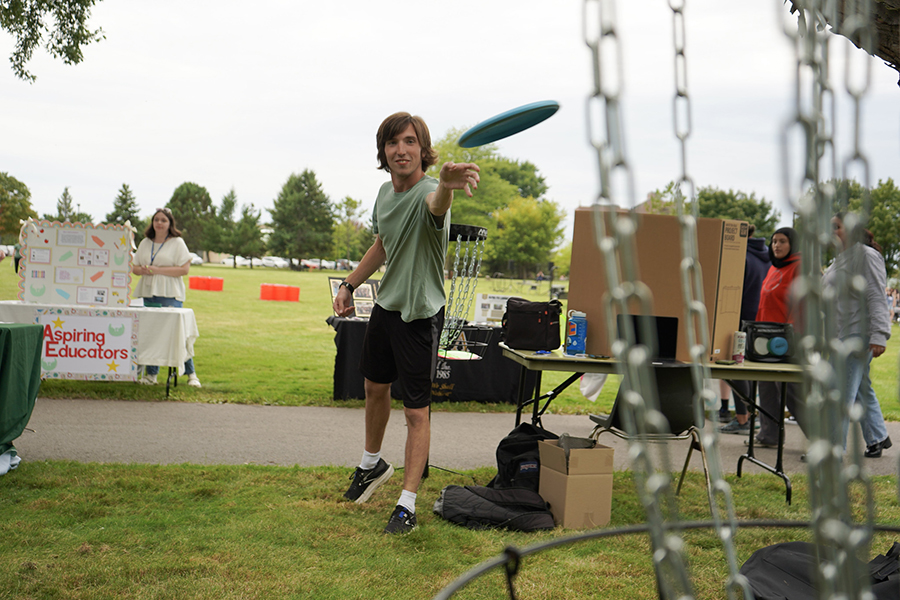 A student throws a frisbee at a disc golf target