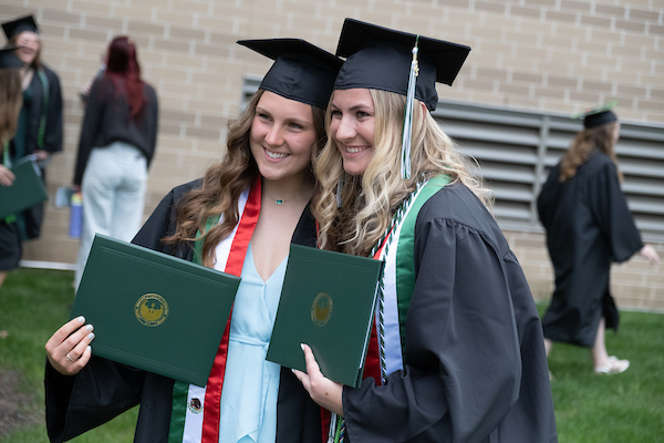 Two female students pose with their diplomas after Commencement