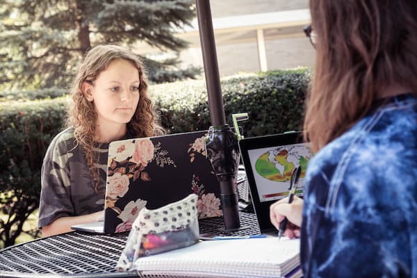 Two female student study on laptops outdoors