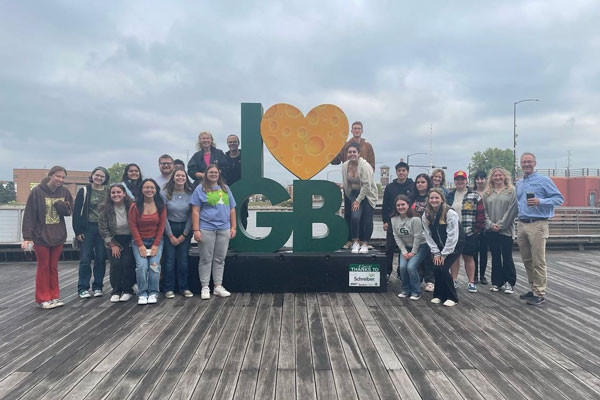 Group of students pose but I love Green Bay sculpture