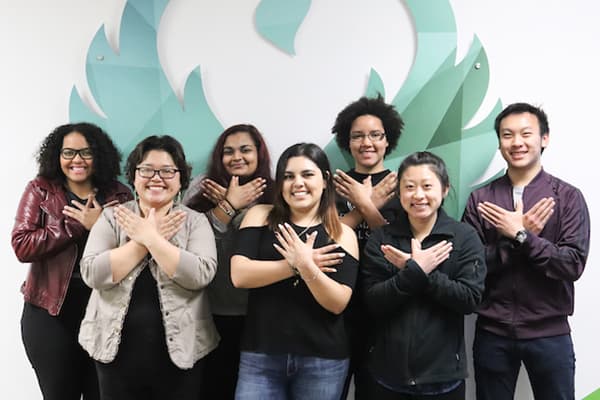 Group of students and Mai Lo Lee flashing the Phoenix hand gesture by the Phoenix Wings photo backdrop