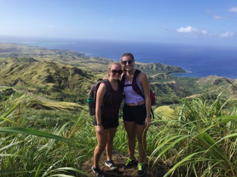 Two backpackers on top of a grassy mountain by the coast