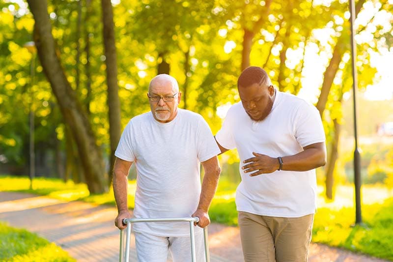 man caregiver walking on outdoor path with patient using walker