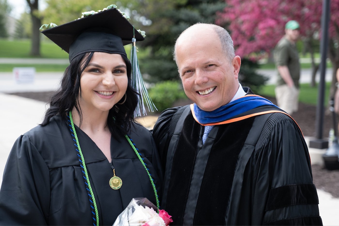A faculty members poses with a graduated student outdoors after the commencement ceremony